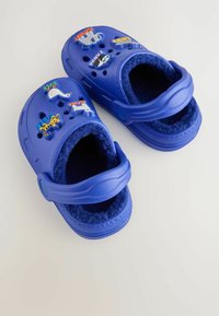 Kék gyerek klumpák puha belsővel, dekoratív állatmintás kitűzőkkel. Szellőzőnyílásokkal és állítható hátsó pánttal tervezve.