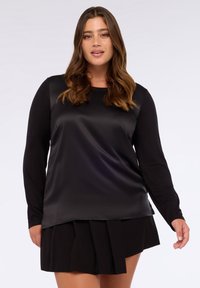 Schwarze Bluse mit langen Ärmeln und Satinfinish, mit lockerer Passform und rundem Ausschnitt, kombiniert mit einem plissierten schwarzen Rock.