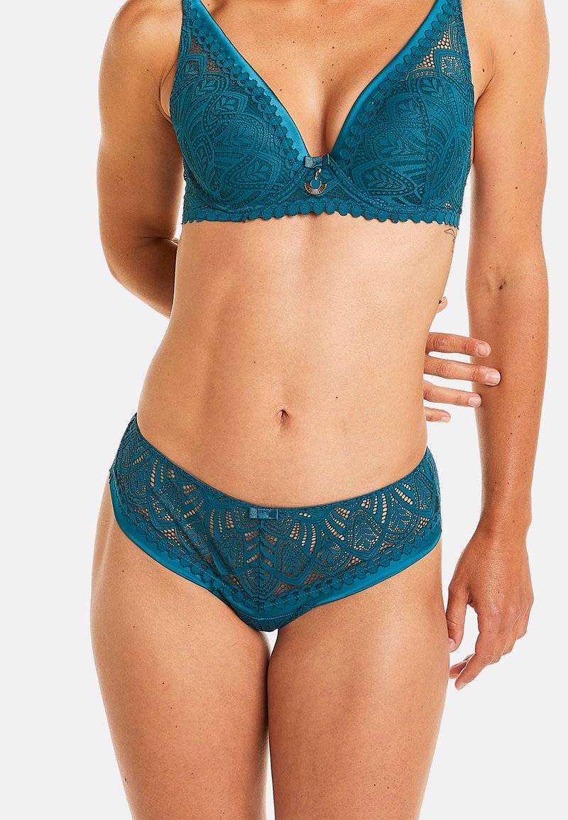 Soutien-gorge en dentelle teal et culotte hipster assortie avec des bords scallopés, présentant des motifs de feuilles complexes et un petit pendentif décoratif.