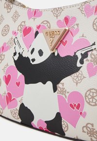 Witte en zwarte neplederen tas met roze hartpatronen, met een zwarte panda graphic die geweren vasthoudt en een gouden driehoekig logo.
