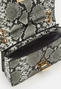 Kabelka s motivem hadí kůže v odstínech šedé a černé se zlatými kovovými doplňky. Interiér je podšitý černou látkou a má magnetické zavírání.