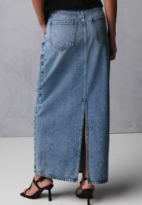 Lys blå denim maxi nederdel med en slids bagpå og to baglommer, samt en frynset kant. Parret med sorte stiletter.