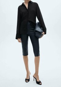 Blusa nera a pois con maniche lunghe, abbinata a pantaloni capri in pelle nera a vita alta e tacchi aperti neri. Inclusa borsa scura.