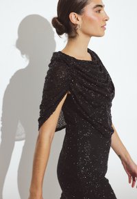 Čierne večerné šaty s drapovaným, textúrovaným živôtikom vyrobeným z trblietavého materiálu, s krátkymi rukávmi a priliehavým strihom.