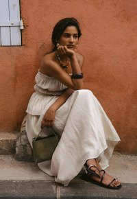 Robe blanche fluide avec un tissu texturé, associée à des sandales noires. Accessoirisée avec un sac à main vert et un collier de perles colorées.