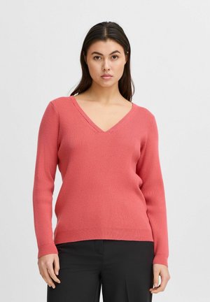 Pull en V côtelé de couleur corail avec des manches longues, associé à un pantalon noir. Le tissu est doux et légèrement ajusté.