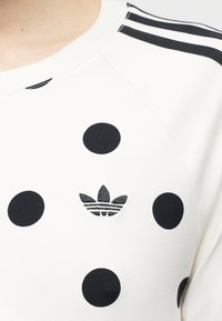 Valge särk mustade täppidega, õlal kolm musta triipu ja must Adidas'i trefoil logo täppide keskel.