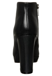 Svart läderankelboot med hög klack, försedd med en dragkedja baktill och kontrasterande sömmar längs sömmarna för extra detalj.
