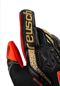 Guante de portero negro con acentos rojos y dorados, que presenta un agarre texturizado, un diseño flexible y una marca en la correa de la muñeca.