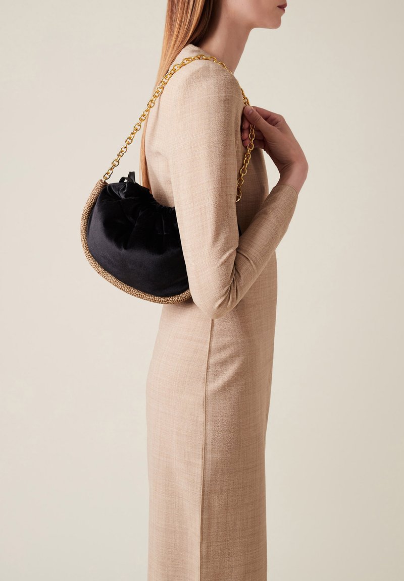 Black velvet handbag with a gold chain strap, accented by a woven beige trim. Rounded shape with a gathered top design.