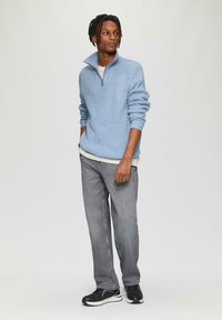 Himmelblauer gestrickter Pullover mit hohem Kragen, graue Jeans mit geradem Bein und schwarze Sportschuhe. Strukturiert, lässig und entspannte Passform.