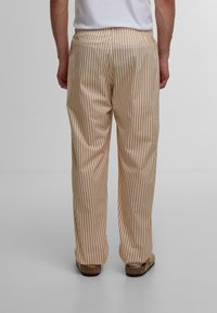 Stripete bukser med en beige og lys brun fargeskala, laget av et glattere materiale, med en avslappet passform og baklommer.