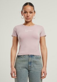 Kortsleeve, tettsittende t-skjorte i myk rosa bomull med rund hals og hvit tekstdesign, kombinert med høyt liv blå denimjeans.