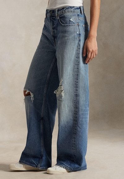 Bredbente blå jeans laget av denim, med slitte rifter på knærne, falmet vask og klassisk femlommers design.
