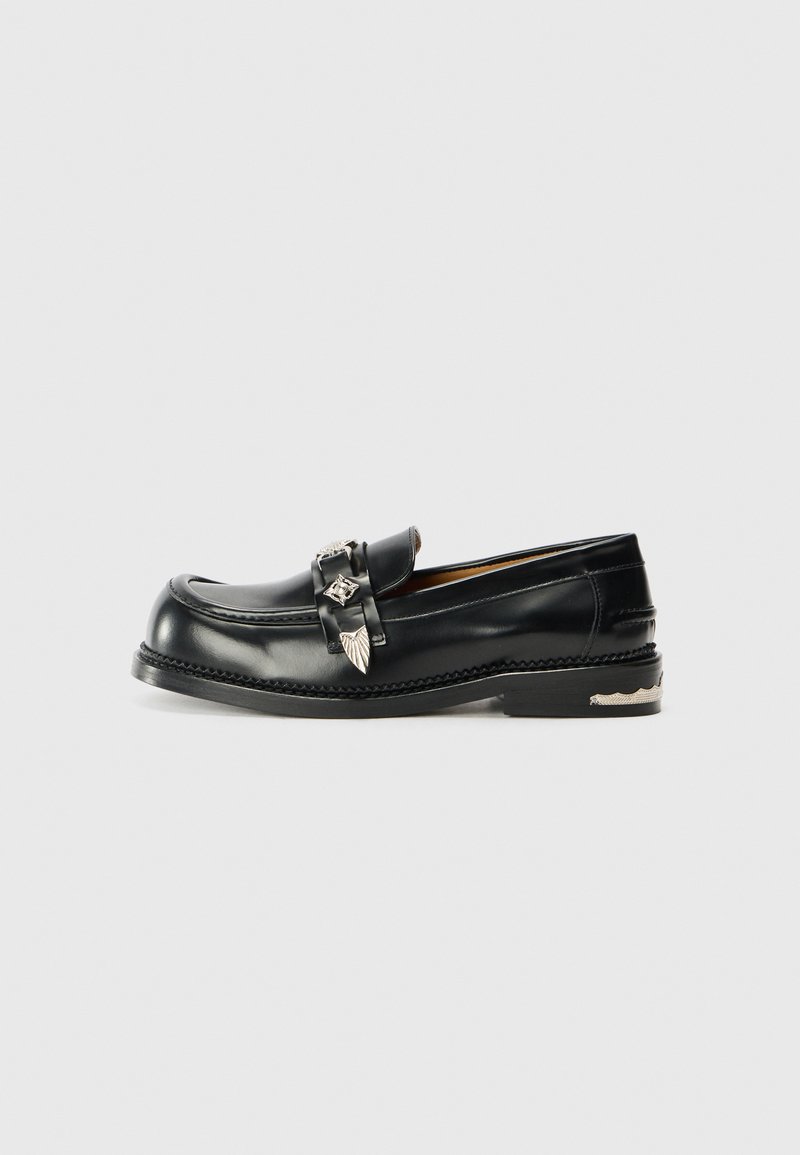 Schwarze Lederloafer mit runder Zehenform, dekorativen Schnallenakzenten und detaillierten Nähten entlang der Außensohle. Flaches Absatzdesign.