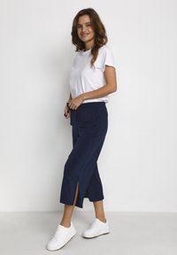 Pantaloni blu navy con fessure laterali, abbinati a una t-shirt bianca semplice e sneakers bianche. Design semplice e rilassato in tessuto morbido.