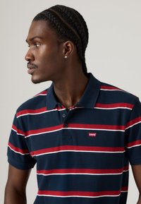 Ναυτικό πόλο μπλούζα με κόκκινες και άσπρες οριζόντιες ρίγες. Διαθέτει κουμπωτό γιακά και μικρό κόκκινο λογότυπο Levi's στο στήθος. Υλικό από βαμβάκι.