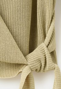 Pulover tricotat bej, cu textură groasă în relief și detaliu cu nod legat la tiv.