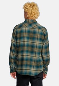 Camicia a maniche lunghe a quadri nei colori marrone, teal e crema. Presenta un colletto classico, polsini con bottone e una vestibilità morbida. Tessuto con motivo testurizzato.