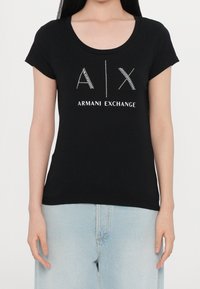 Camiseta negra de manga corta con cuello redondo y texto blanco brillante "A|X ARMANI EXCHANGE" impreso en el frente.