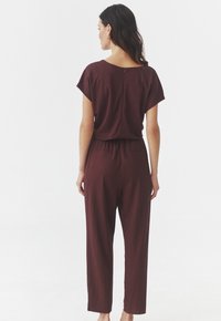 Bordeaux jumpsuit van zachte stof, met korte mouwen, een relaxte pasvorm, elastische taille en een rits aan de achterkant voor sluiting.