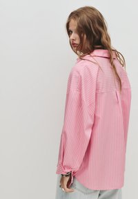 Camicia a righe rosa con una vestibilità rilassata, dotata di un collo a camicia e bottoni sui polsini. Tessuto liscio, materiale leggero.