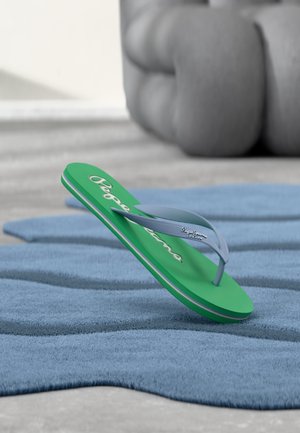 Tongs vertes et grises Pepe Jeans reposant sur une surface bleue ondulée texturée avec des éléments gris flous en arrière-plan.