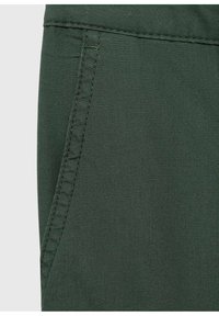Dark green fabric featuring a side pocket with contrasting stitching. Smooth texture and a fitted design are notable features.