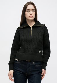 Černý pletený svetr s vysokým límcem na zip a texturovaným vzorem. Má žebrované manžety a lem a vyšívané logo na přední straně.