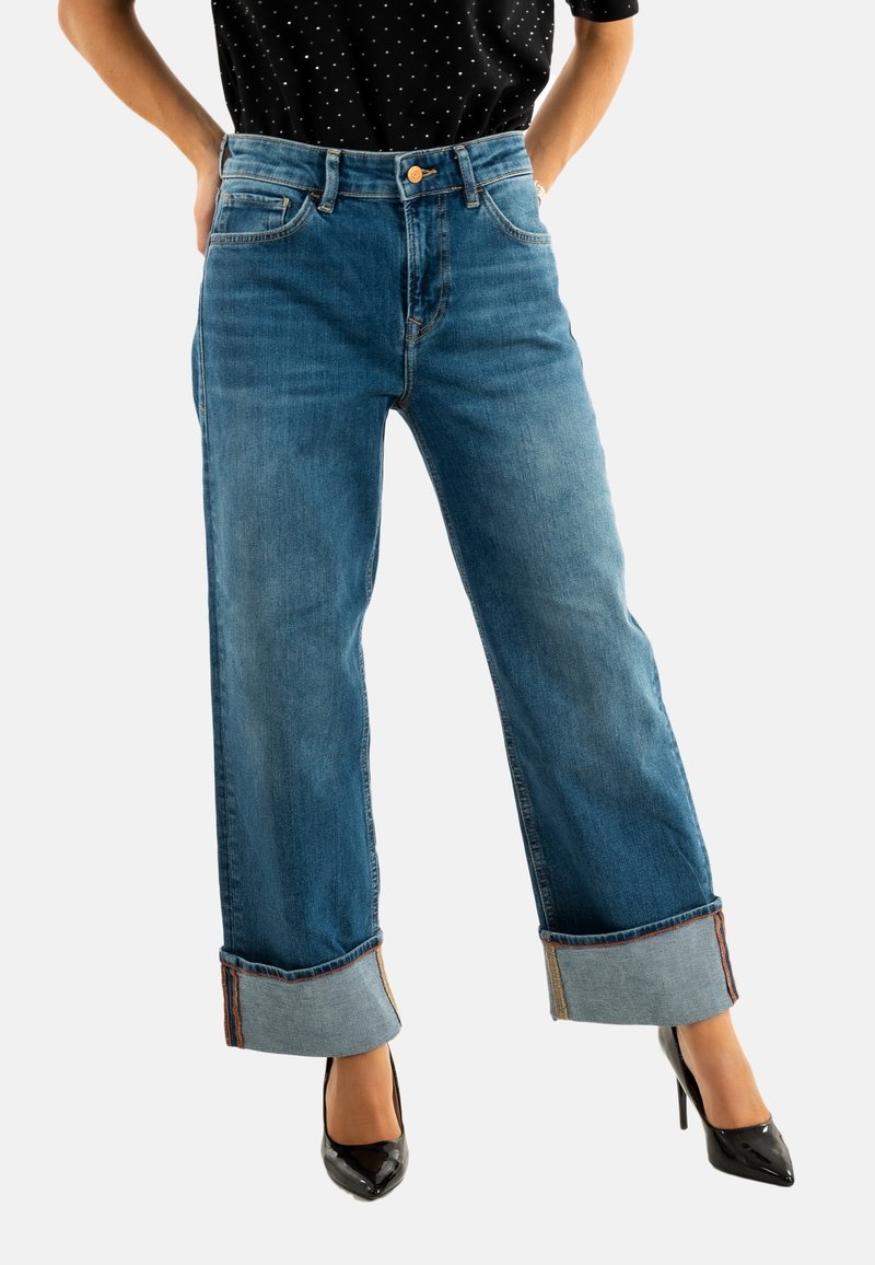 Jeans blu a vita alta con vestibilità rilassata, orli risvoltati e dettagli in contrasto sulle cuciture interne, abbinati a tacchi alti neri.