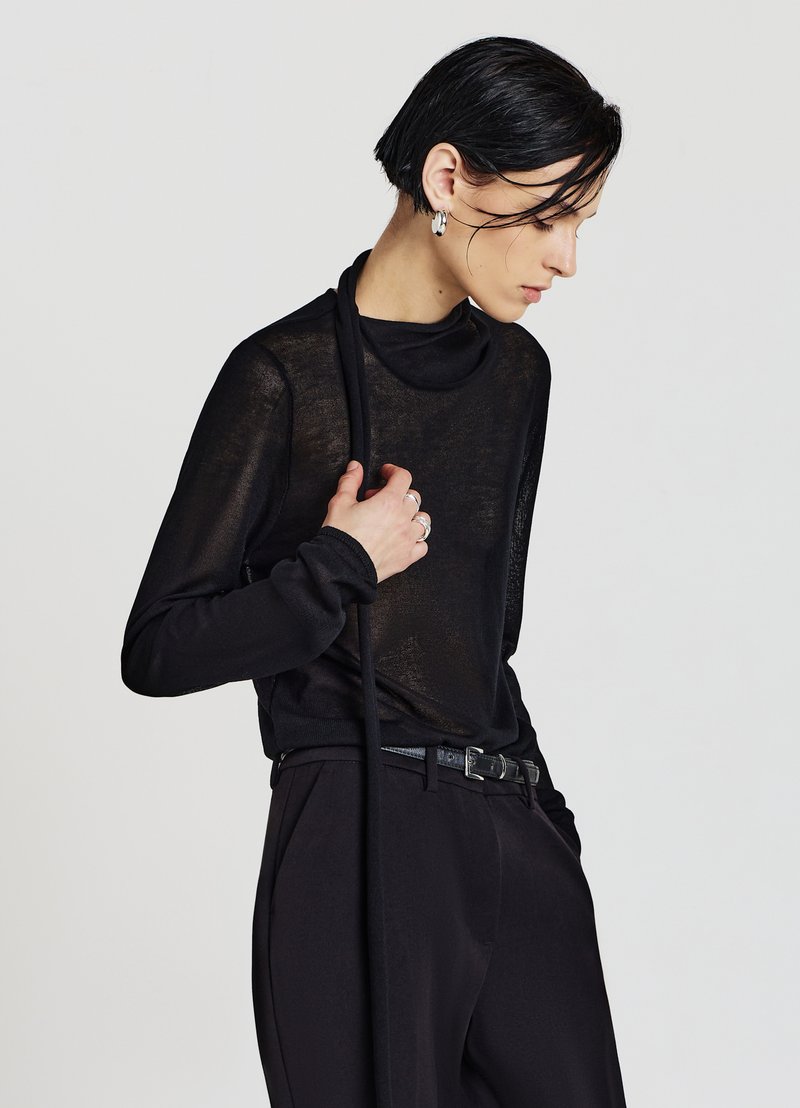 Haut noir à manches longues en tissu transparent avec un col montant. Associé à un pantalon noir et une ceinture fine. Surface texturée avec un éclat subtil.