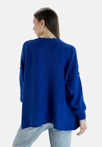 Suéter de punto azul de gran tamaño con un acabado texturizado, puños acanalados y una silueta relajada, combinado con jeans de mezclilla claros.