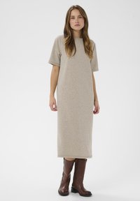 Bežs jersija maxi kleita ar īsām piedurknēm, taisnu griezumu un apaļu kakla izgriezumu, kombinēta ar brūnām ceļgala augstām zābakiem. Gluda tekstūra.