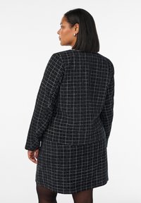 Schwarz-weiße karierte Anzugjacke mit langen Ärmeln, strukturiertem Stoff, tailliertem Schnitt und quadratischem Muster, getragen mit einem passenden Rock.