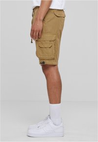 Beige cargoshorts med flera fickor och justerbar knytning i midjan. Bärs med vita sneakers och vita crewsockor. Enfärgad bakgrund.