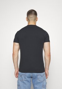 Camiseta corta negra de algodón, con un clásico cuello redondo. El fondo es blanco liso, lo que resalta el color de la camiseta.