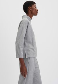 Grijze oversized sweatshirt met een hoge kraag, zijsplitten en brede mouwen. Gemaakt van gebreide stof met een zachte textuur. Gecombineerd met bijpassende broek.
