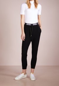 Czarne dresy z elastycznym paskiem i sznurkiem, z białym logo, połączone z dopasowaną białą bluzką i białymi trampkami. Gładka tekstura materiału.