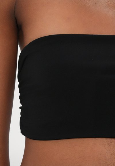 Melnas strapless kroplokjas augšdaļa, kas izgatavota no gludas, stiepjamas auduma ar saskaitāmām detaļām sānos. Vienkāršs, bezšuvju dizains bez redzamām aizdares.
