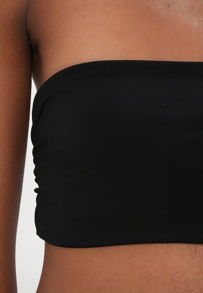 Svart strapless crop top i slät, elastisk tyg med rynkade detaljer på sidorna. Enkel, sömlös design utan synliga knäppningar.