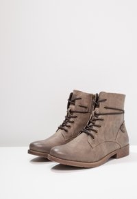 Botas tobilleras grises con un upper sintético texturizado, diseño con cordones, ojales en tono dorado y un tacón bajo apilado. Cierre lateral para una fácil puesta.