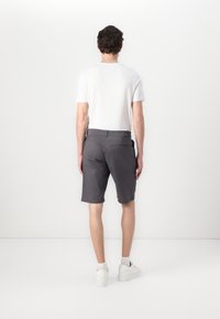 Graue Shorts aus Stoff, mit geradem Schnitt, seitlichen Taschen und einer Gesäßtasche, kombiniert mit einem weißen T-Shirt mit kurzen Ärmeln und weißen Sneakers.