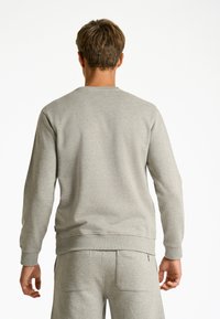 Grå sweatshirt med rund hals och långa ärmar; slät textur och ribbade cuffs, kombinerad med matchande byxor med bakfickor.