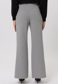 Vrouw in hoge taille, zwart-wit geblokte wijde broek en zwart lange mouwen top, staand met handen langs haar zij.