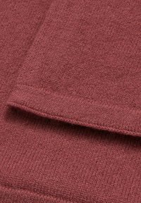 Tissu tricoté de couleur rouille avec une texture fine, présentant un bord replié et une surface lisse et uniforme.