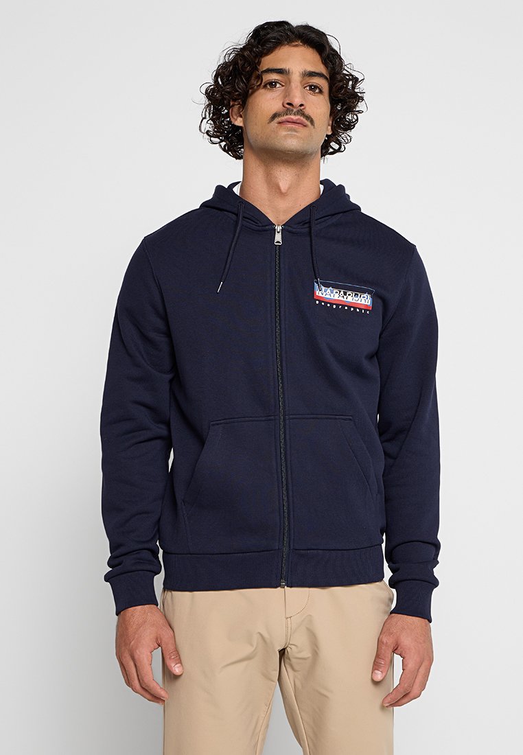 Marinefarbener Zip-Hoodie aus einem Baumwollmischgewebe, ausgestattet mit einer Fronttasche, einer Kapuze mit Kordelzug und einem kleinen Logo-Patch in Rot und Blau.