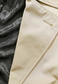 Tissu beige avec une texture lisse, combiné avec un tissu noir brillant présentant un motif subtil. Comprend des coutures et un détail décoratif.