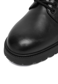 Black leather shoe with rounded toe, thick treaded rubber sole, and black laces, shown from close-up front angle.