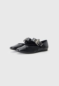 Schwarze flache Schuhe aus Synthetikleder mit einer spitzen Zehe, einer flexiblen Sohle und einem verstellbaren Riemen mit einer silbernen Schnalle.