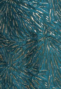 Texturerat tyg med en teal bakgrund och metalliska silverlinjer som liknar abstrakta löv eller vågor.